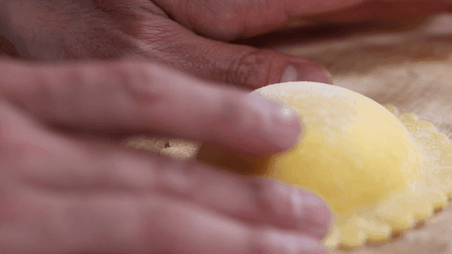 Hands shaping fresh ravioli on a wooden board