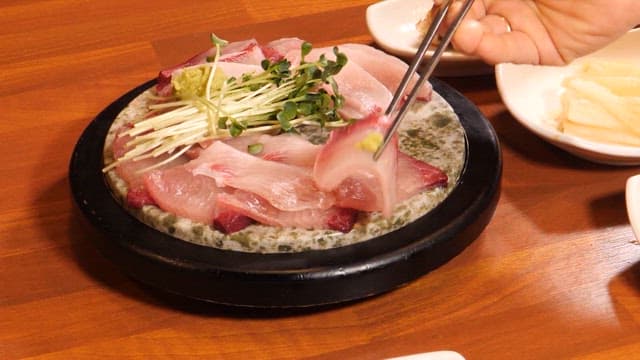 Yellow tail sashimi being dipped in soy sauce