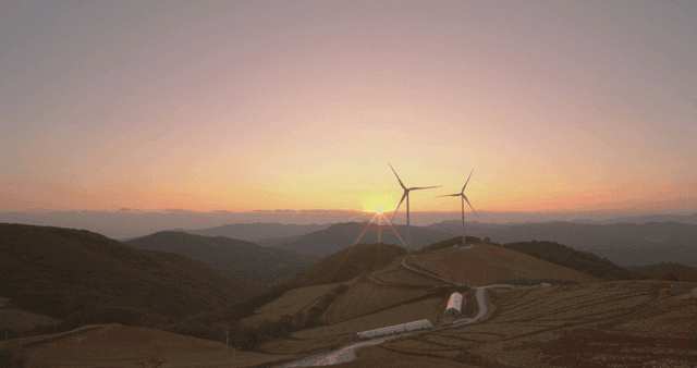 일출에 밭이 있는 언덕 위의 풍력 터빈
