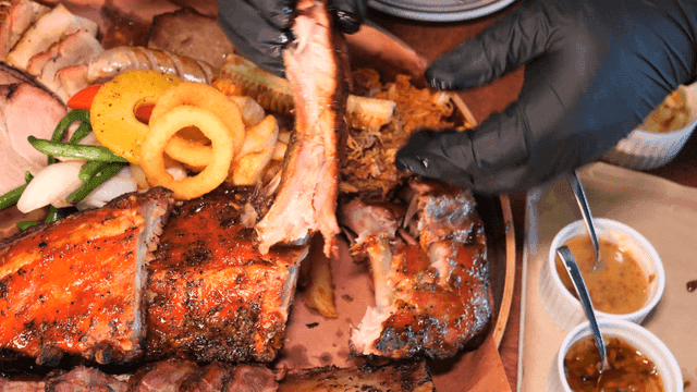 Gloved hand tearing apart barbecue rib