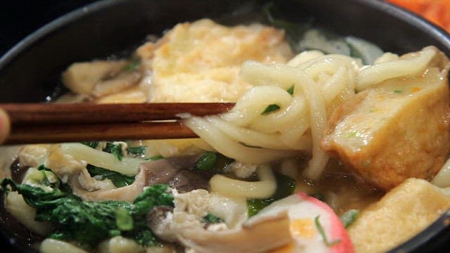 Chopstickful of udon noodles with vegetables and fish cake