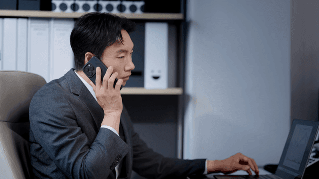 A man cheering while making a phone call in his office