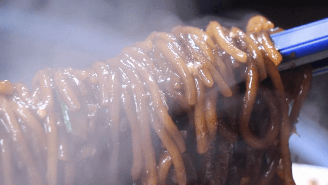 Steaming hot noodles in black bean sauce being lifted