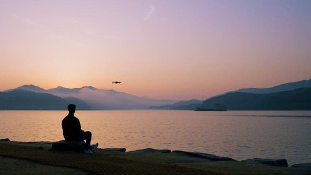 Person Flying a Drone on the Lakeside at Sunrise