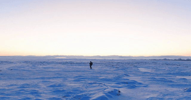 Person walking on a snowy field at sunrise