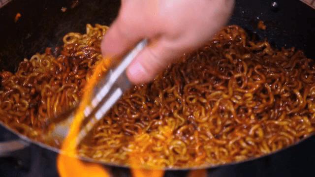 Stir-frying noodles in a pan with flames