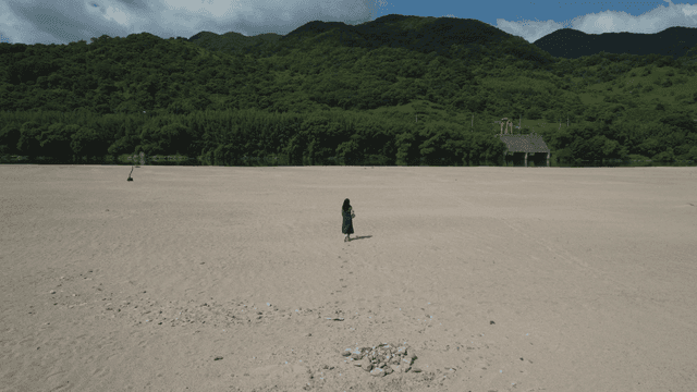 높은 산 아래 넓은 모래밭을 걷는 여성