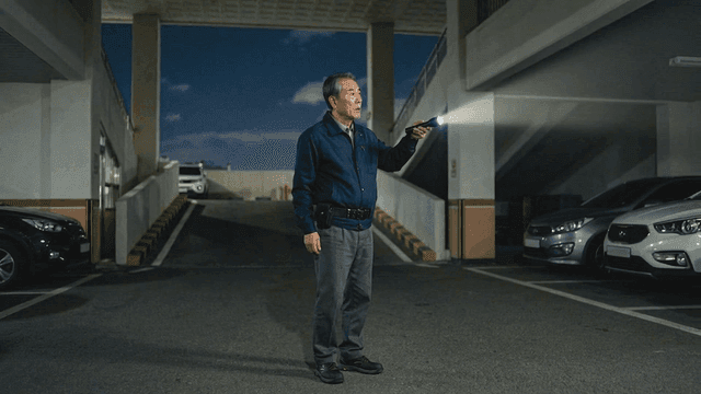 Elderly security guard holding flashlight in parking lot