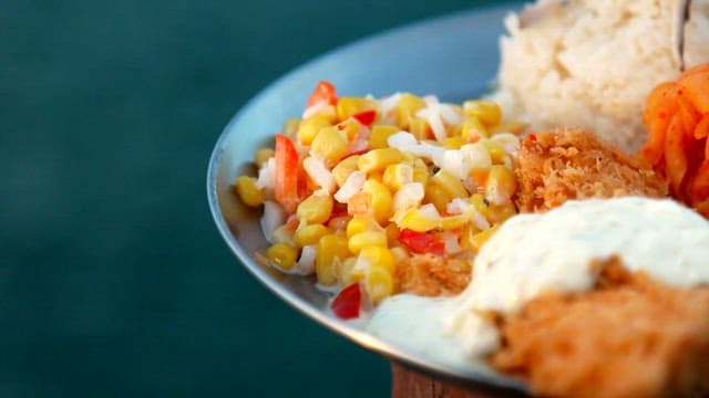 Metal plate with pork belly, corn salad, kimchi, and fried fish