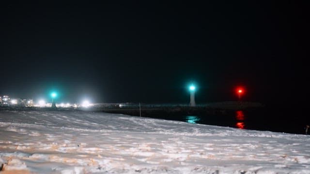 Nighttime scene of a snowy beach with brightly lit lighthouses