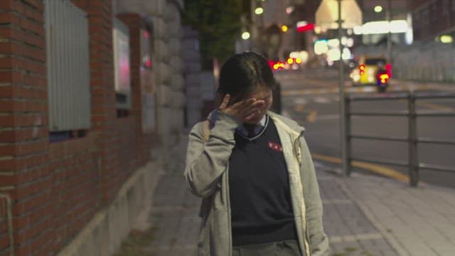 Female student in school uniform wiping away her tears in sadness on a quiet street