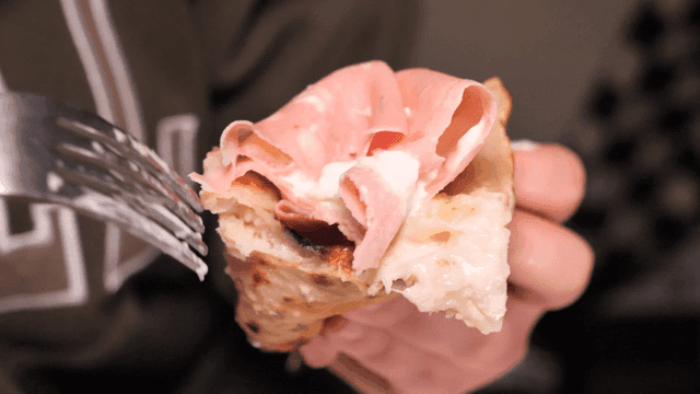 Person holding mortadella pizza with ham