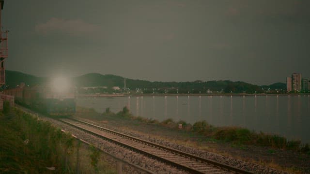 Passenger train traveling beside a serene lake while the sun sets in the background