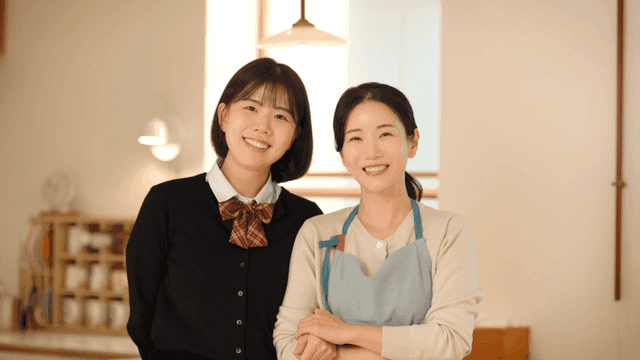 Mother and daughter smiling while looking straight ahead in cozy home