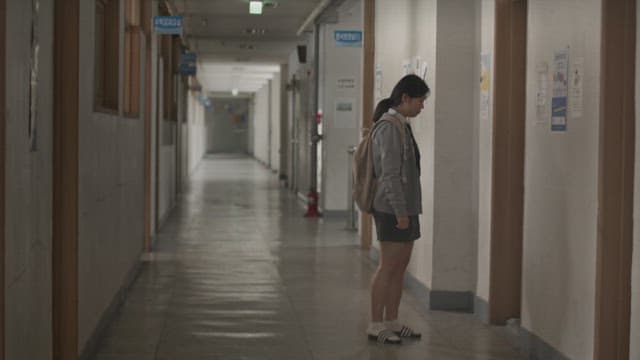 Student standing alone in a dim hallway, looking at the door