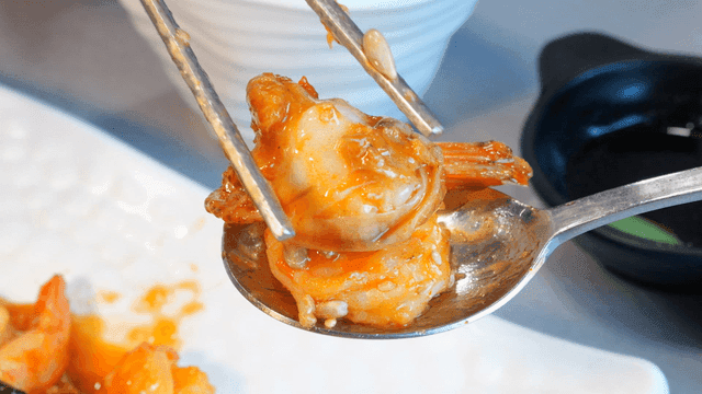 Stir-fried shrimp and red scallops coated in sauce on spoon