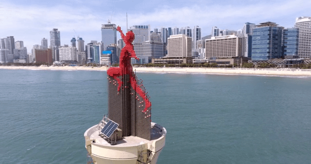 A red statue near a coastal city skyline