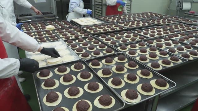 Workers preparing dough pastries filled with red bean paste in a kitchen