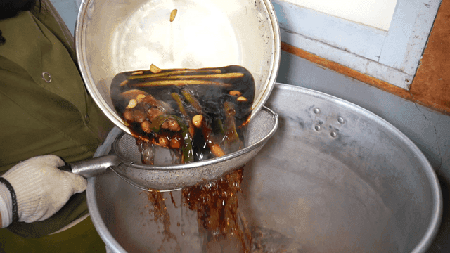 Chef straining soy sauce and pouring it into pot