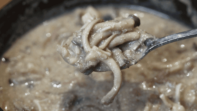 Spoon scooping out perilla seed soup with mushrooms