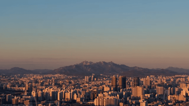 멀리 산이 보이는 도시 전경에 석양이 내려앉은 모습
