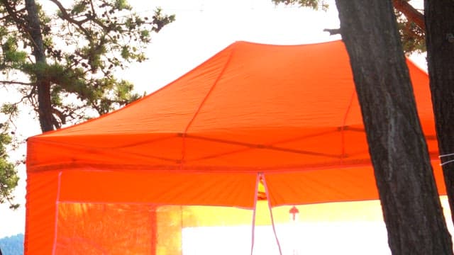 Person setting up an orange outdoor tent on a sunny day