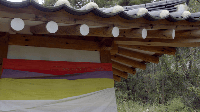 Hanok eaves and colorful tent over shrub forest