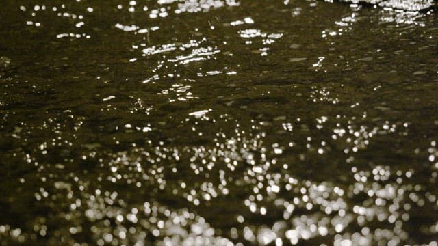 Raindrops splashing on a water puddle at night