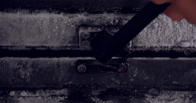 서리가 낀 창문의 걸쇠를 열고 닫는 손