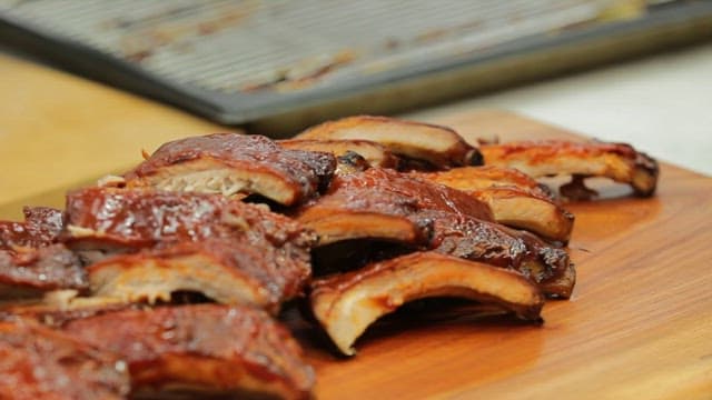 Drizzling sauce over deliciously grilled ribs on a wooden cutting board