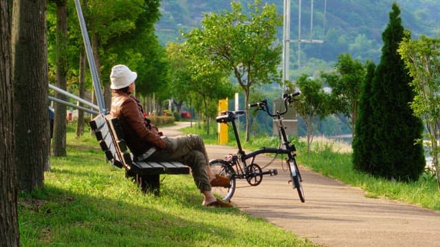 Man relaxing on a bench with a bicycle by his side in a scenic park during the day