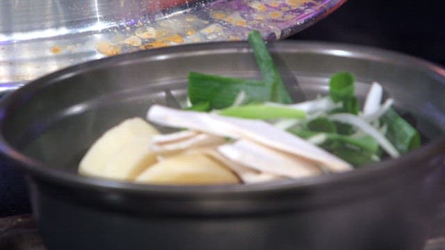 Pouring broth into a pot containing various ingredients