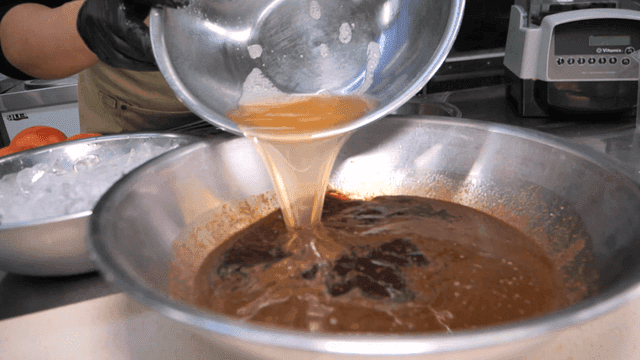 Chef pouring broth into large mixing bowl