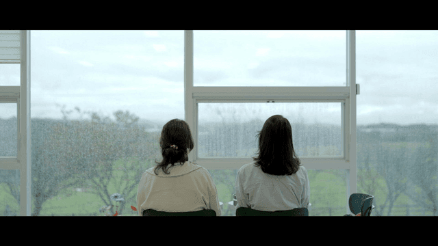 Backs of two women sitting by window on rainy day