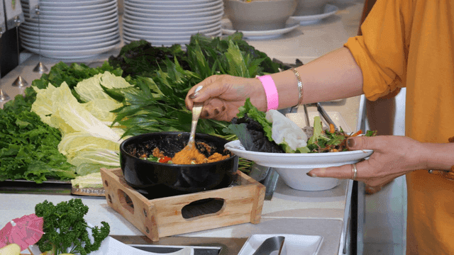 Person placing leafy greens and ssamjang on plate