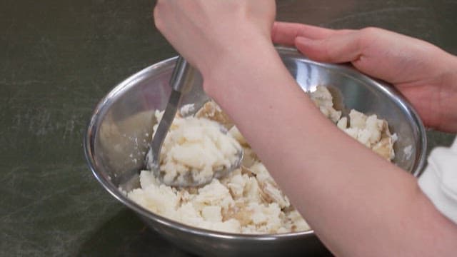 Mashing Potatoes with a Ladle in a Metal Bowl