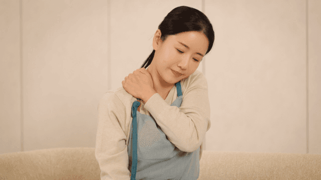 Woman sitting on a sofa holding her shoulder