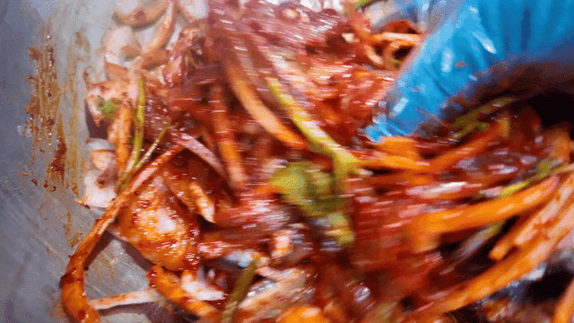 Glove-wearing hands mixing spicy anchovy sashimi salad