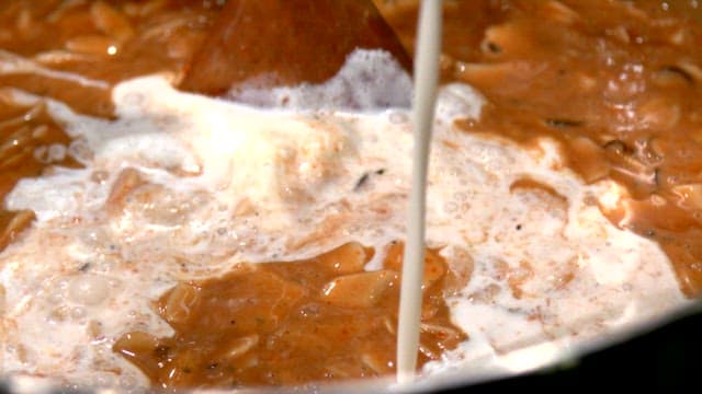 Whipping cream being poured into a simmering tomato sauce