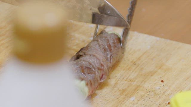 Slicing a meat rolls with green onions on a cutting board