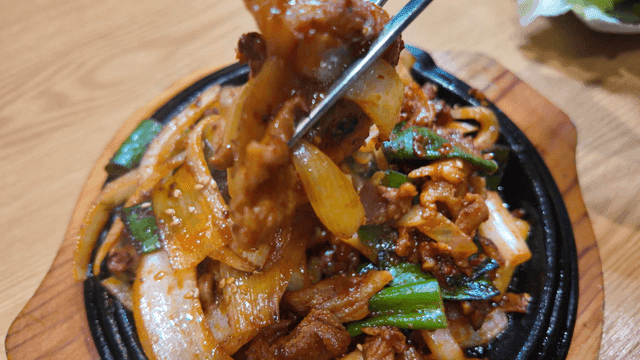 Chopsticks picking up spicy stir-fried pork with vegetables