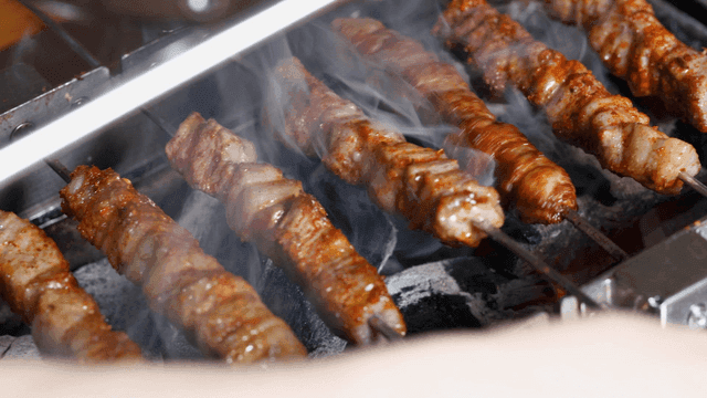 Lamb skewers rotating and grilling over charcoal
