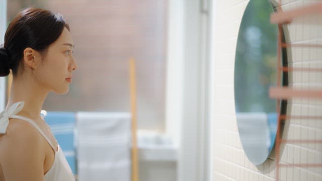 Woman smiling and touching face in front of mirror indoors