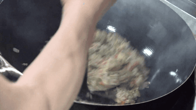 Fried rice being cooked with vegetables in a hot wok