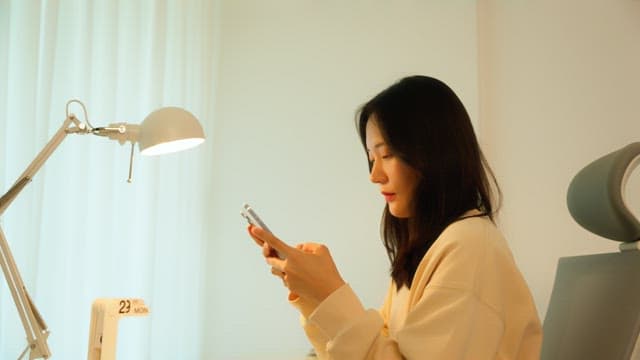 Woman using a smartphone at a desk in a calmly lit room