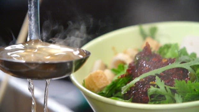 Pouring the broth into a bowl with the fish cakes and spicy sauce