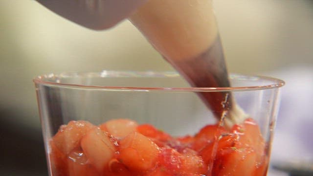 Whipped cream being added to a fruit cup