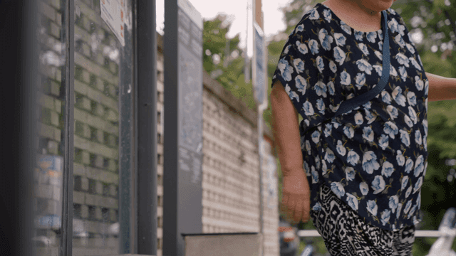 An elderly woman standing up from a bus stop bench