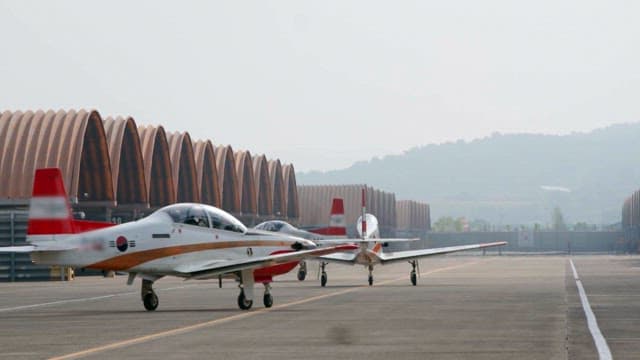 Military aircrafts taxiing on airport runway near hangars