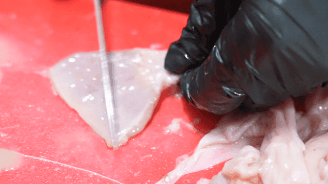 Hands trimming raw chicken offal on red cutting board